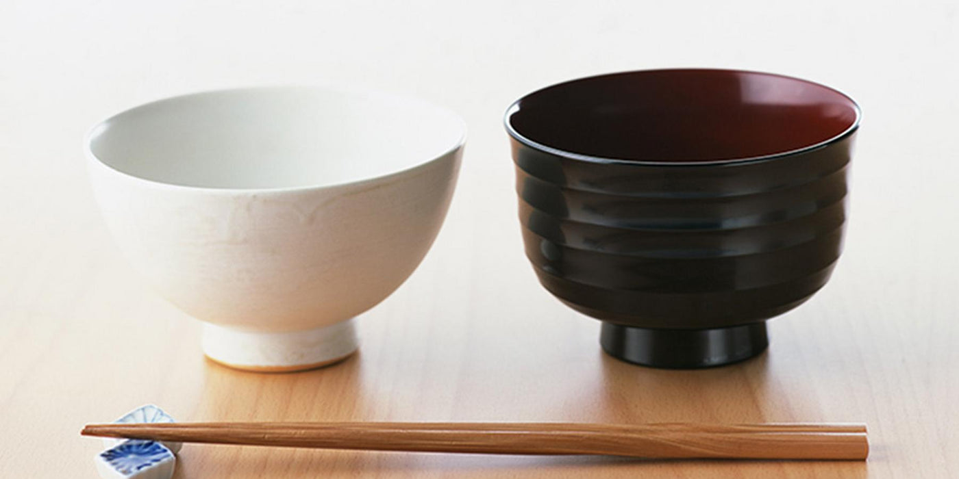 A white rice bowl, a Japanese soup bowl and a pair of wooden chopsticks on a dining table