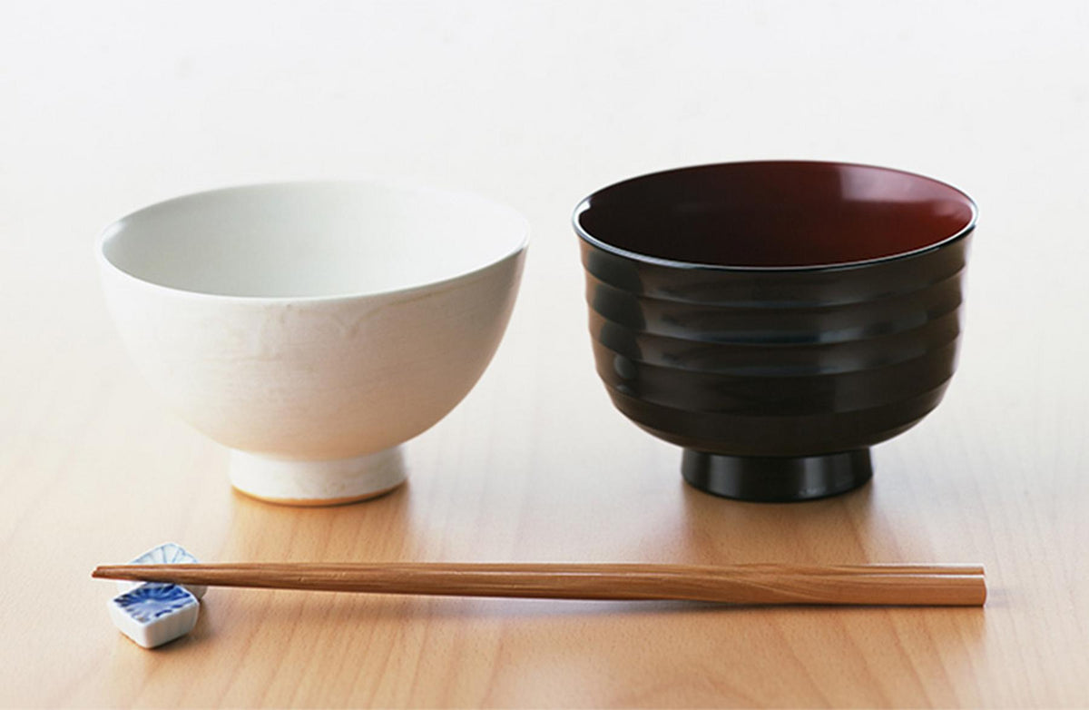 A white rice bowl, a Japanese soup bowl and a pair of wooden chopsticks on a dining table
